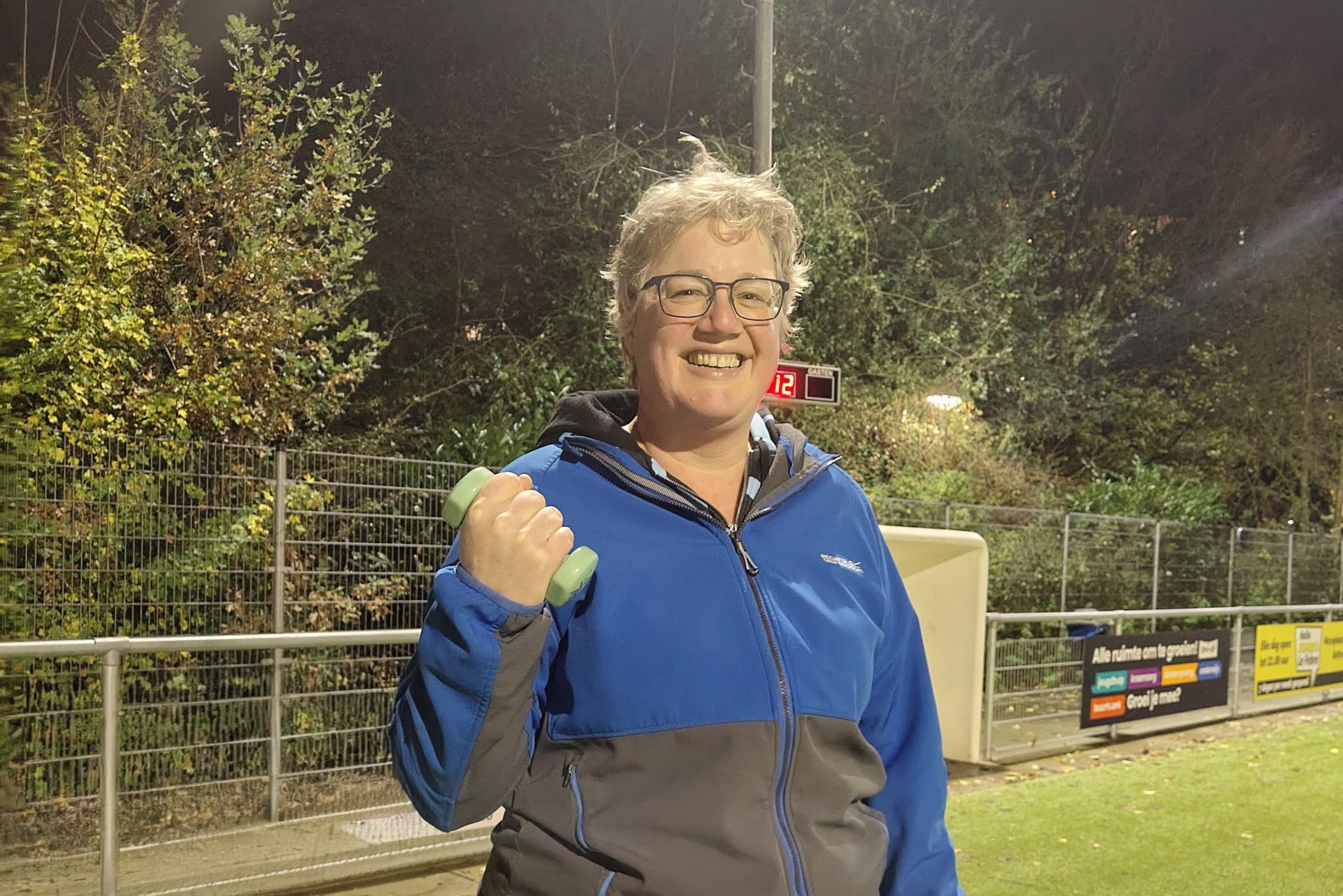 Barbera staat op een sportveld, dat zie je aan de reclameborden die er langs de kant staan, het kunstgras en de digitale klok boven een mini dug out. Ze houdt een blauw gewichtje in haar vuist omhoog en lacht naar de camera. Het is donker maar de lampen staan aan.